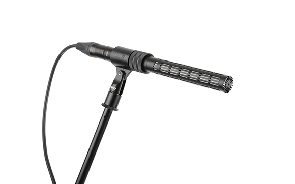 A black shotgun microphone mounted on a boom stand against a white background.