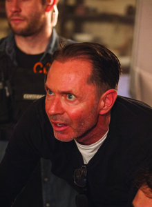 A man with short dark hair and blue eyes looks off-camera with a wide-eyed, surprised expression.