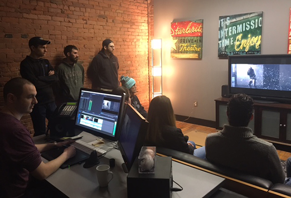 People in a room with brick walls watching a video on a large television screen.