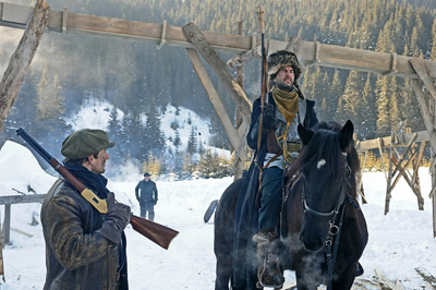 A man on a dark horse and another man holding a rifle stand in a snowy mountain landscape.