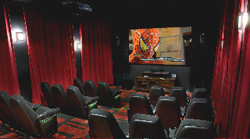 A private home cinema with red velvet curtains, black leather seats, and a large screen playing an animated film.