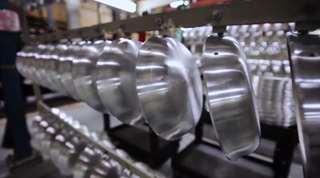 A row of shiny, silver metal bowls moving along a conveyor belt in a factory.