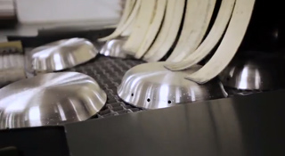 Silver metal dome-shaped parts and long curved strips on a dark industrial conveyor belt.