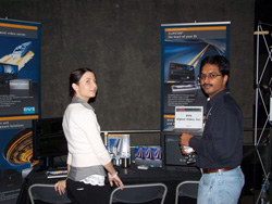 A woman and a man stand behind a table with promotional banners and products displayed.