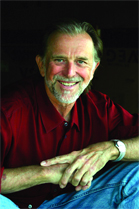 A smiling man with graying hair and a beard wearing a red button-down shirt.