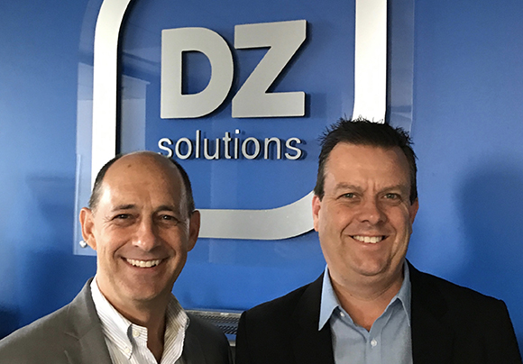 Two men in business attire smiling in front of a blue wall with a DZ solutions logo.