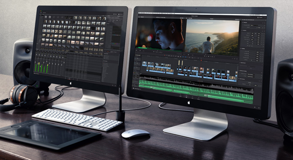 Two computer monitors displaying video editing software on a desk with speakers, headphones, and peripherals.
