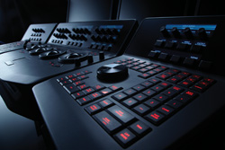 Close-up of dark professional audio mixing consoles with illuminated buttons and knobs in a dim studio.