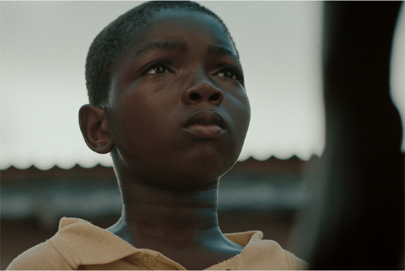 Close-up of a young Black boy looking upward with a thoughtful, serious expression against a blurred background.