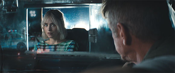 A blonde woman looks toward a man from outside a vehicle at night.