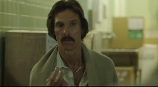 A man with dark hair and a mustache wearing a light-colored shirt and jacket.