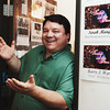 A smiling man in a green short-sleeved shirt gestures with both hands open.