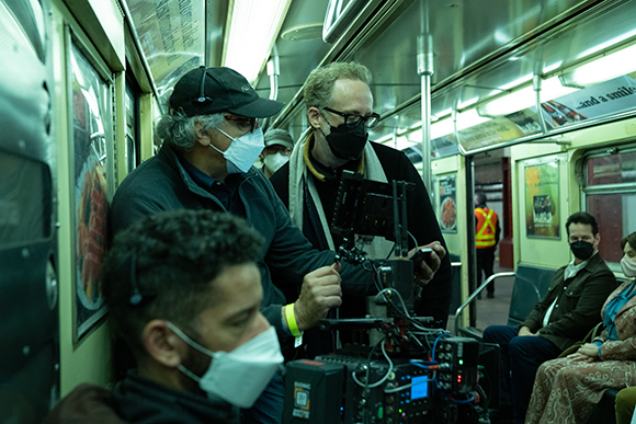 Film crew with cameras and equipment filming inside a green subway car.