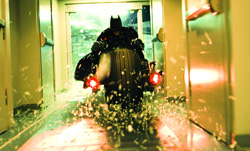 A person in a dark bat-themed costume riding a motorcycle through a brightly lit hallway.
