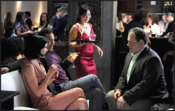 A group of people talking and drinking in a dimly lit lounge setting.