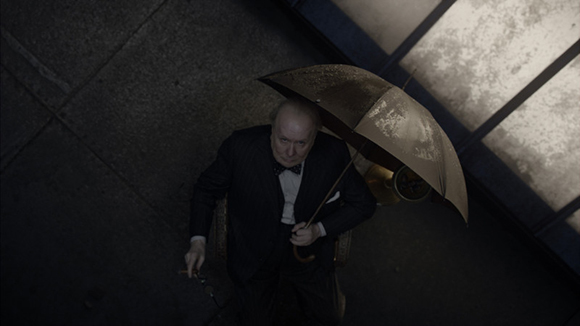 High angle view of an elderly man in a dark suit holding a large umbrella.