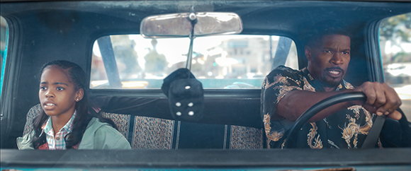 A man with a worried expression drives a car while a young girl looks on from the passenger seat.