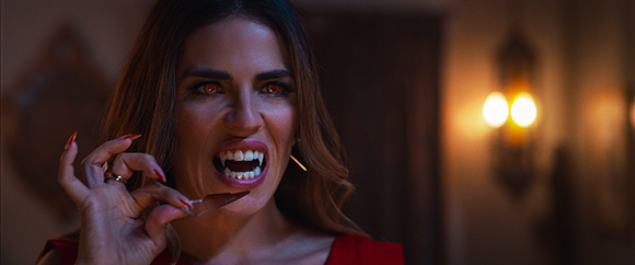 A woman with long hair, glowing orange eyes, and sharp vampire fangs baring her teeth.