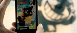 A person holds a smartphone showing a colorful digital collage in front of a blurred background.