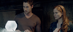 A man and a woman stare intently at a glowing, white octagonal object in a dark room.