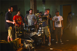 A group of crew members stand around a professional camera rig on a dolly in a dark room.
