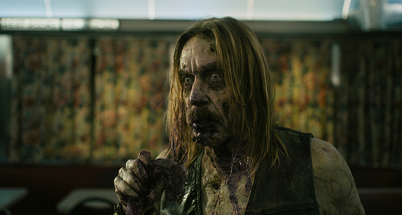 A person with disheveled hair and blood-stained skin stares intensely forward in a dimly lit setting.