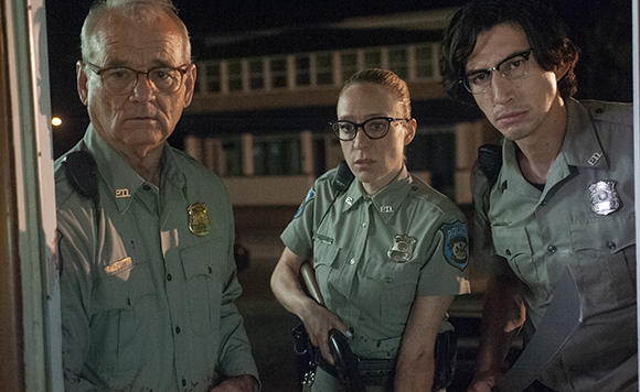 Three officers in light green uniforms stand outdoors at night with serious expressions.