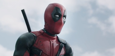 A person in a red and black superhero mask and suit looking to the side against a cloudy sky.
