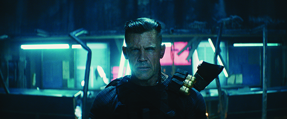A man with short hair and a serious expression stands before glowing blue and pink neon lights.