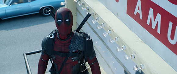 A person in a red and black Deadpool superhero suit stands next to a white sign with light bulbs.