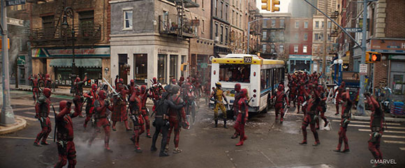 Many figures in red combat suits stand in a city street around a white and yellow bus.