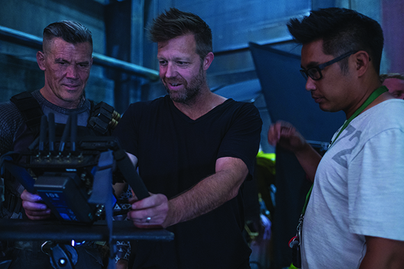 Three men on a film set looking down at a camera monitor in a dimly lit studio.