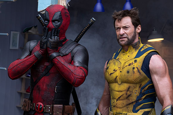 Deadpool in a red suit covers his mouth while Wolverine in a yellow suit looks forward.