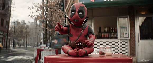A Deadpool plush toy sits on a red table in an outdoor urban setting.