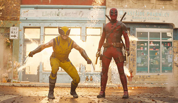 Wolverine in a yellow suit and Deadpool in a red suit stand in a street with sparks flying behind them.