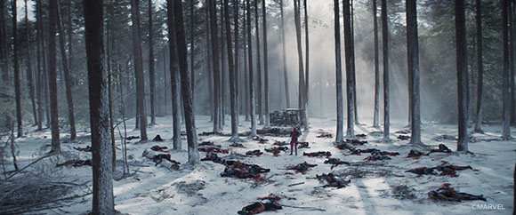 A person stands in a snowy forest surrounded by many fallen bodies on the ground.