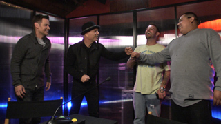 Four men standing in a room, laughing and gesturing toward each other.