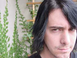 Close-up of a man with long dark hair looking forward against a background of climbing green vines.