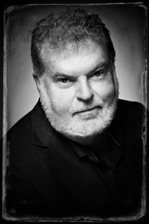 Black and white portrait of a man with short hair and a full beard wearing a dark jacket.