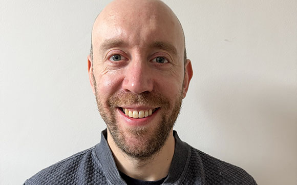 A smiling bald man with a short beard looking directly at the camera against a plain white background.