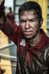 A man with a dirt-streaked face and dark hair wearing a stained red work shirt.