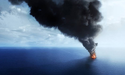 A large, dark plume of smoke billows from a bright orange explosion on the surface of a blue ocean.