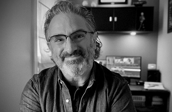 Black and white portrait of a smiling man with glasses and a salt-and-pepper beard in an office setting.