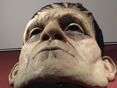 A large, detailed mask of a monster's face with pale skin, dark hair, and sunken eyes.