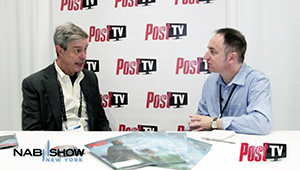 Two men sit at a table talking in front of a white backdrop with red Post TV logos.