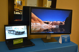 A laptop showing a car and a large monitor displaying a landscape under a starry sky on a blue tablecloth.