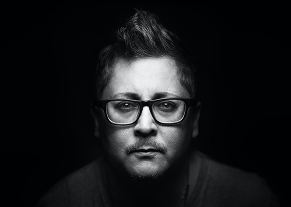 Black and white close-up portrait of a man with glasses looking directly at the camera.
