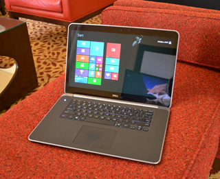 A silver Dell laptop open on a red textured couch, displaying the Windows Start menu.