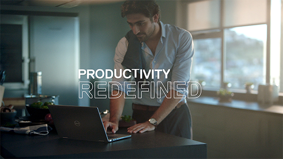A man in a light blue shirt works on a laptop at a kitchen counter.