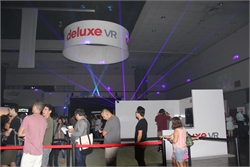 People stand in line at a Deluxe VR booth. Laser lights are projected across the ceiling.